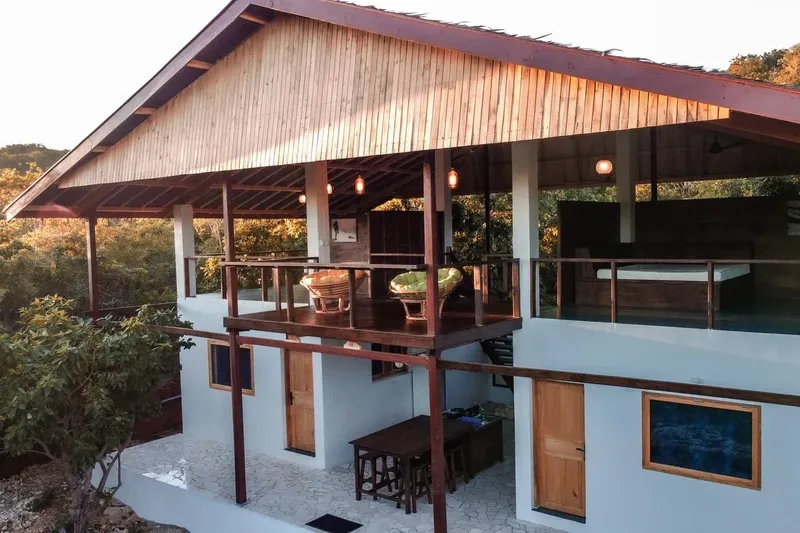 Bâtiment blanc et bois avec balcon, végétation luxuriante en arrière-plan