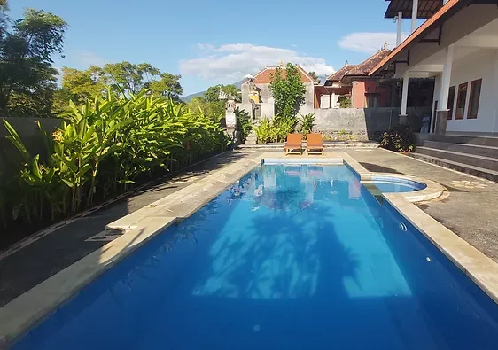 Piscine rectangulaire bleue entourée de végétation et de bâtiments blancs