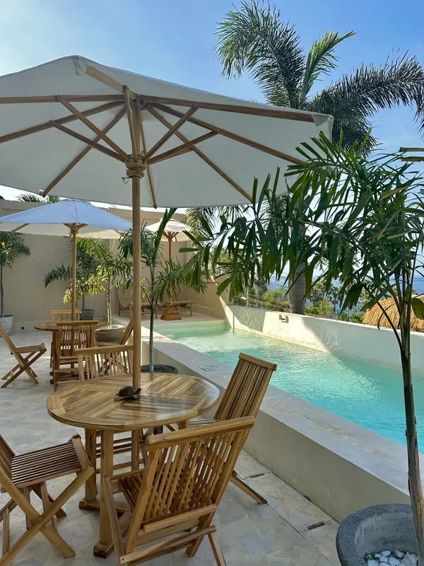 Terrasse avec tables, chaises, parasols et piscine au bord d'une végétation tropicale