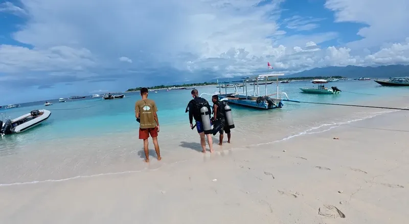 Plongée : deux personnes équipées marchent sur une plage ensoleillée