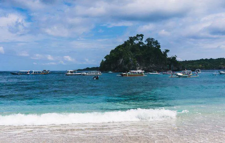 Plage tropicale avec bateaux de pêche et petite île rocheuse