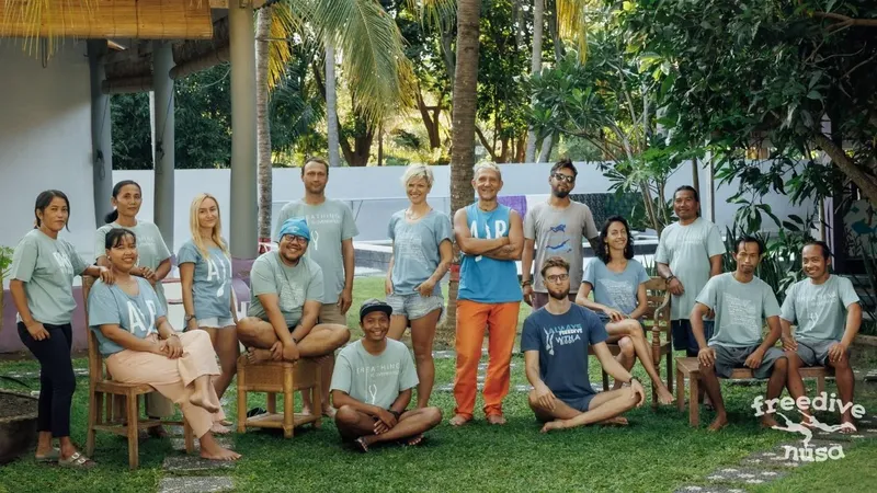 Groupe de personnes souriantes posant devant une maison tropicale verdoyante