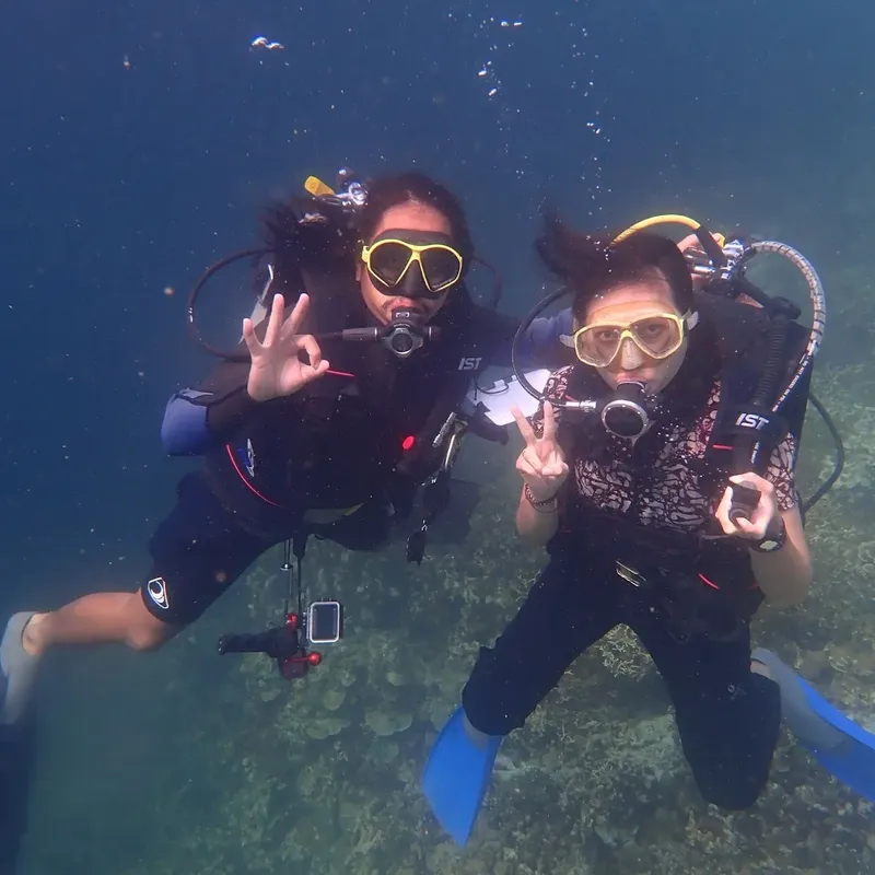 Deux plongeuses souriantes font un signe de la main sous l'eau
