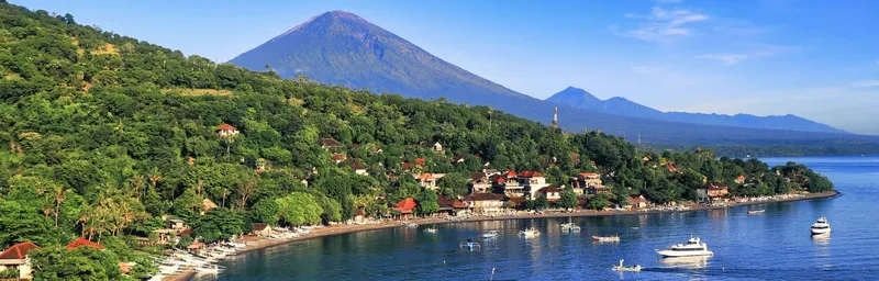 Paysage côtier avec végétation luxuriante, bateaux et montagne en arrière-plan