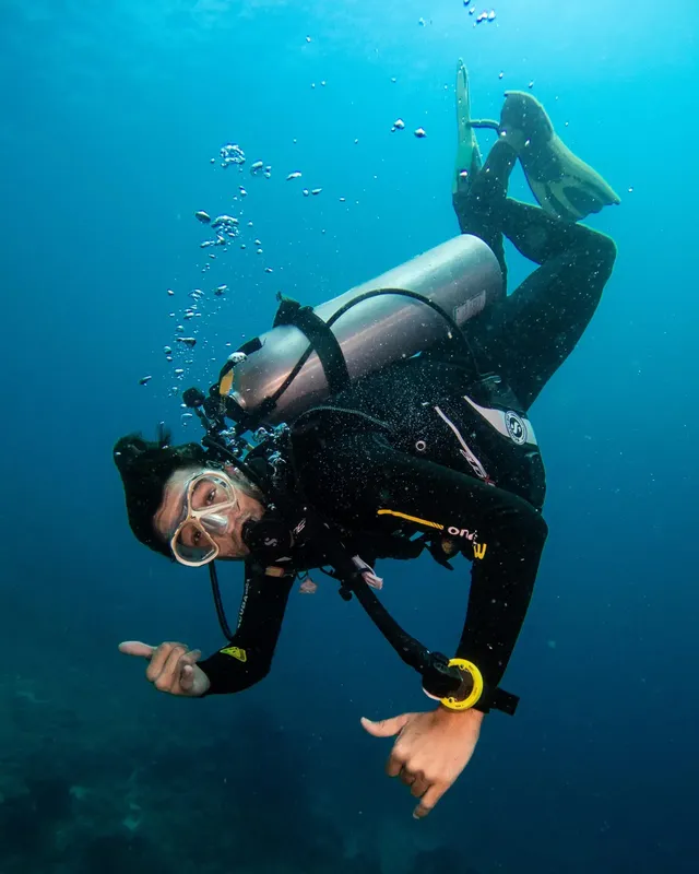 Plongeur en combinaison pointant vers le spectateur dans l'eau bleue