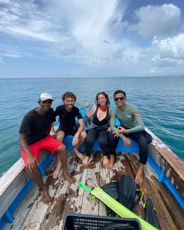 Quatre personnes souriantes sur un bateau de pêche, équipement de plongée visible