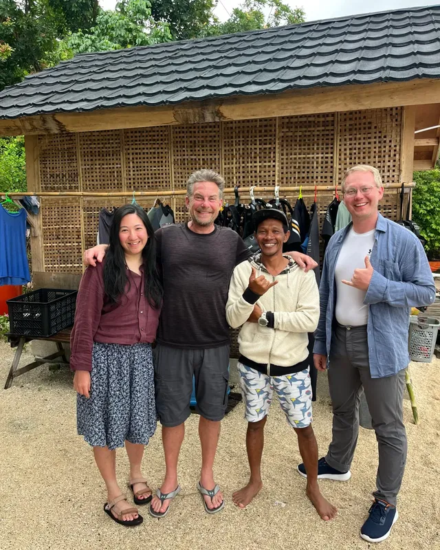 Quatre personnes souriantes posent devant un bâtiment et du matériel de plongée