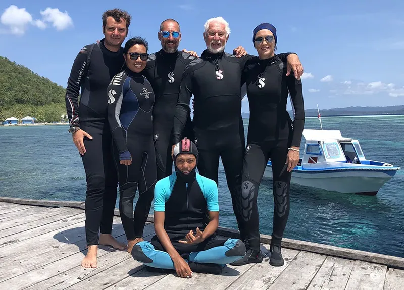 Groupe de plongeurs souriants posant sur un ponton ensoleillé