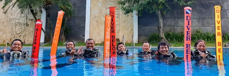 Groupe de plongeurs souriants en formation dans une piscine avec bouées