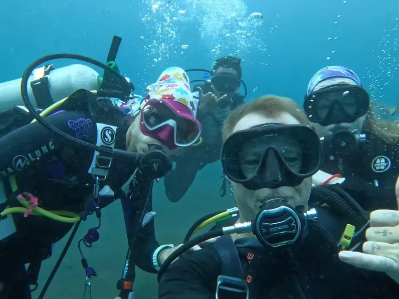 Groupe de plongeurs souriants, équipés, dans une eau claire et bleue