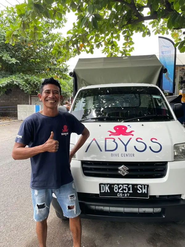 Homme souriant devant un van de plongée blanc avec le pouce levé