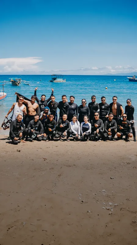 Groupe de plongeurs souriants sur une plage ensoleillée avec bateaux en arrière-plan