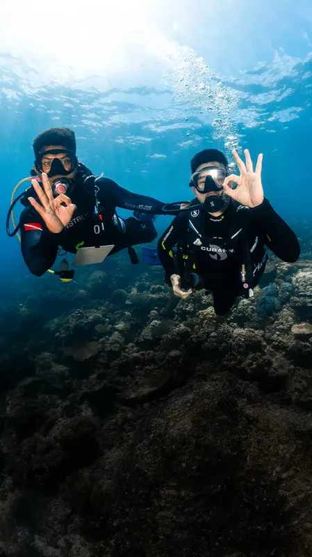 Deux plongeurs souriants font des signes positifs au fond marin