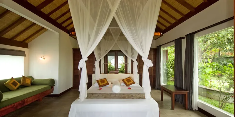 Chambre avec lit à baldaquin, canapé vert et vue sur la végétation