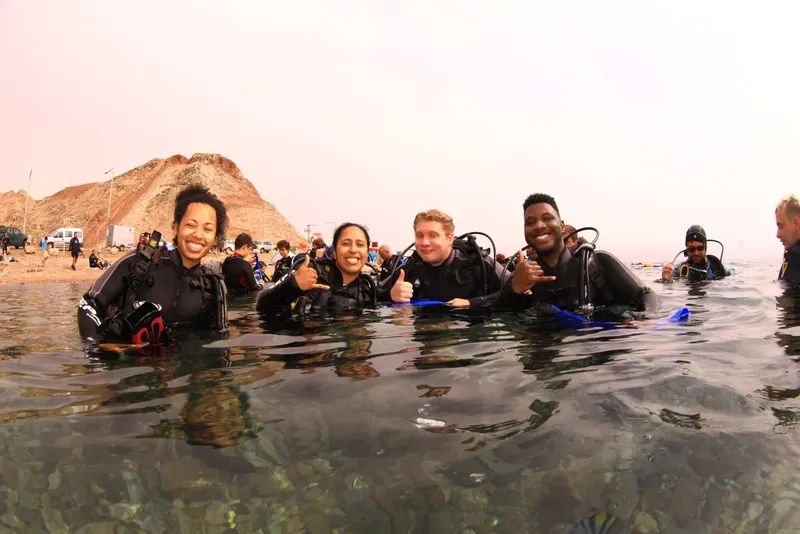 Groupe de plongeurs souriants dans l'eau peu profonde sur une plage