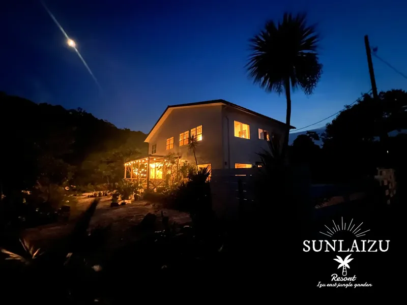 Bâtiment éclairé la nuit avec végétation luxuriante et logo du resort