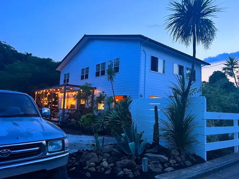 Maison blanche éclairée avec jardin tropical et voiture garée devant