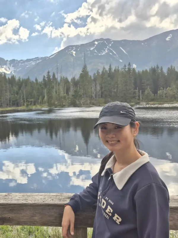 Jeune femme souriante devant un lac de montagne et des sapins
