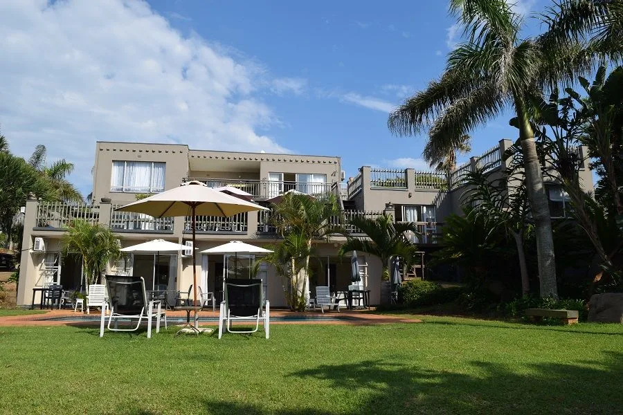 Bâtiment beige avec parasols et pelouse verte sous ciel bleu