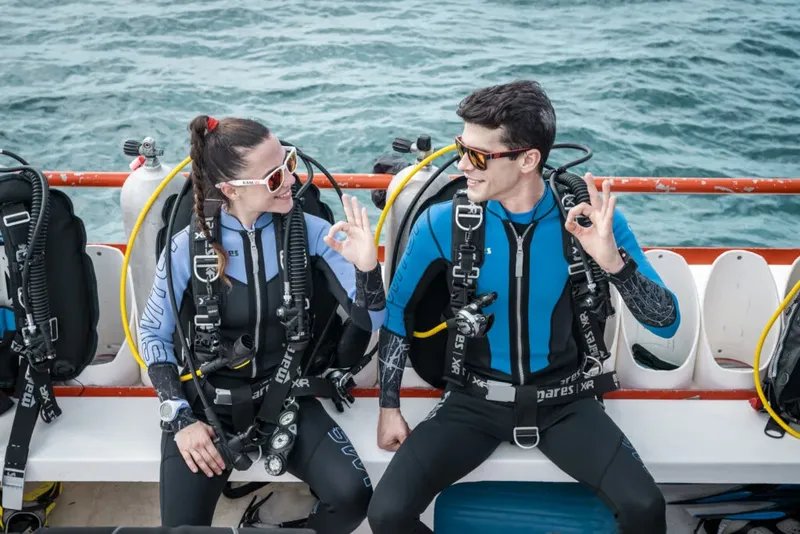 Deux plongeurs souriants sur un bateau, équipés et prêts à plonger