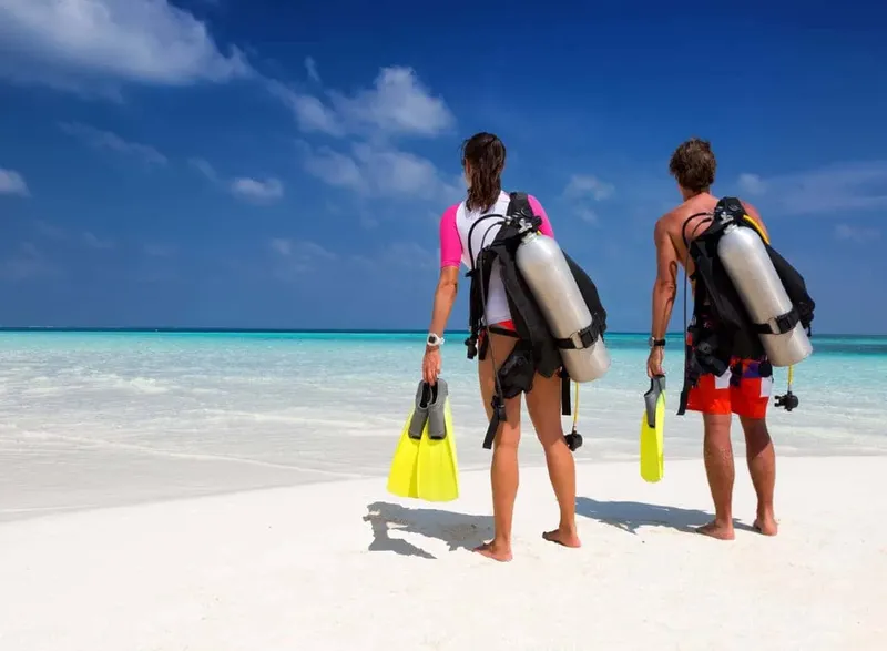Deux plongeurs équipés regardent l'océan turquoise depuis une plage de sable blanc