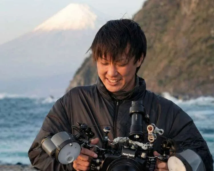 Un plongeur souriant manipule un appareil photo sous-marin sur une plage