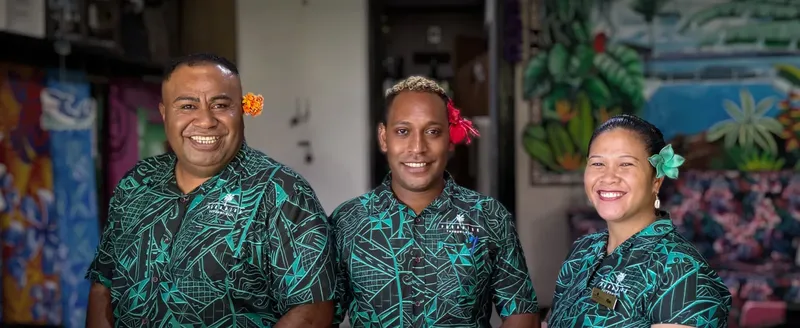 Trois personnes souriantes, portant des chemises à motifs tropicaux et fleurs