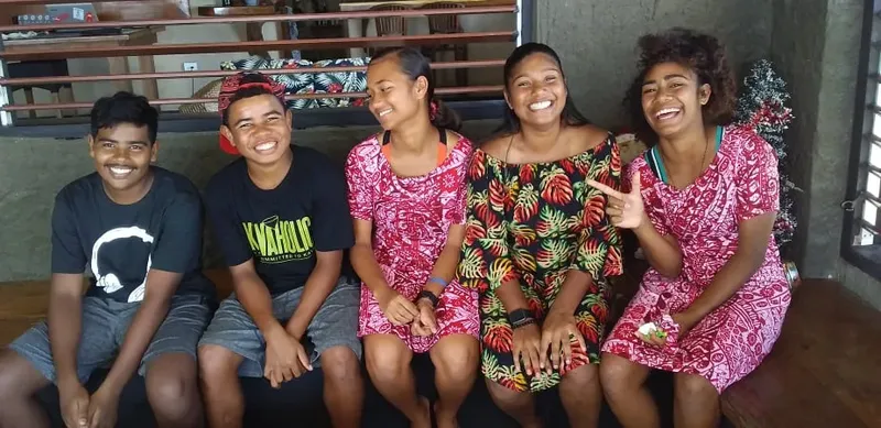 Groupe de cinq jeunes souriants assis sur un banc en intérieur