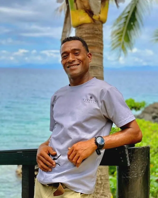 Homme souriant appuie ses mains sur une rambarde face à la mer