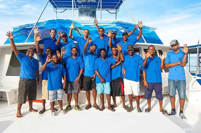 Equipe souriante salue depuis le pont d'un bateau de plongée bleu