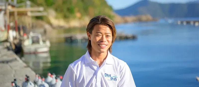 Jeune homme souriant près de bouteilles de plongée et de bateaux