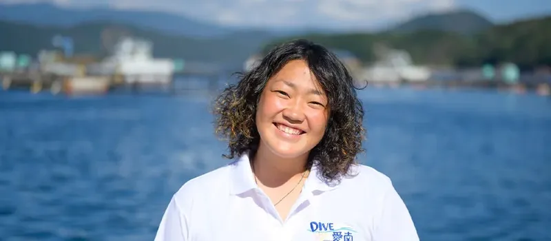 Femme souriante devant la mer et des bateaux amarrés au port