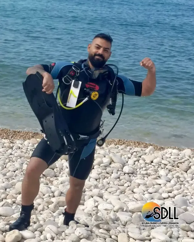 Plongeur en combinaison sortant de l'eau sur une plage de galets