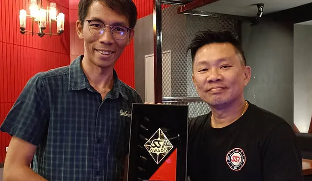 Deux hommes souriants posent avec un trophée noir et rouge