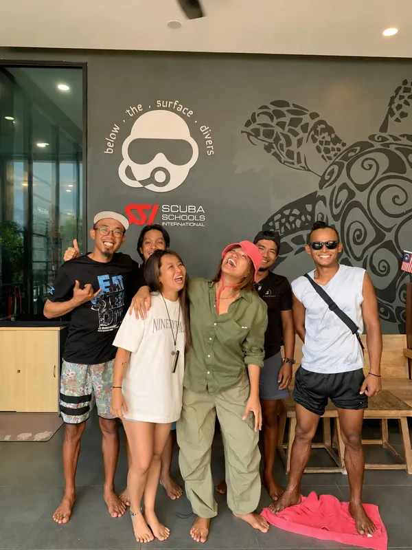Groupe de personnes souriantes devant un mur décoré d'un masque