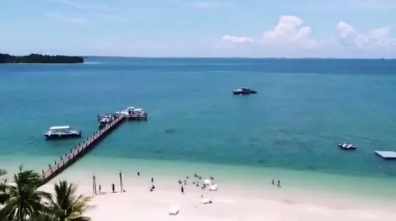 Plage de sable blanc avec des personnes et bateaux en mer
