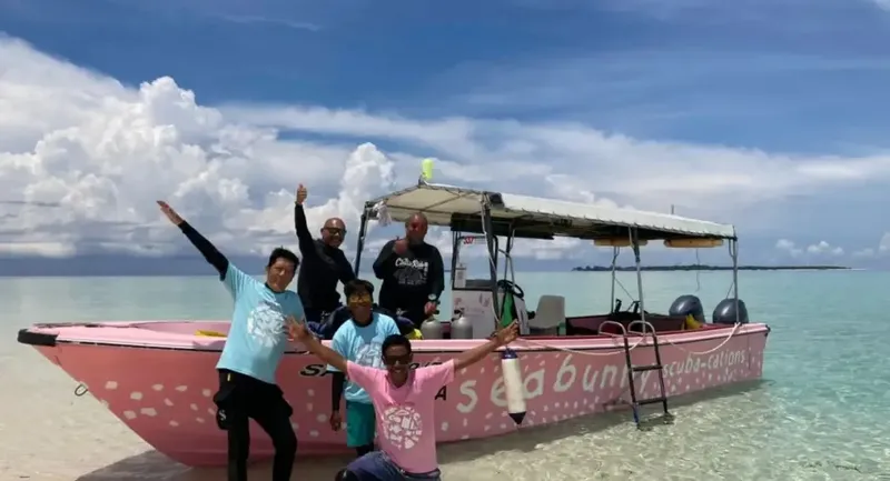 Groupe de personnes souriantes sur un bateau de plongée rose en mer