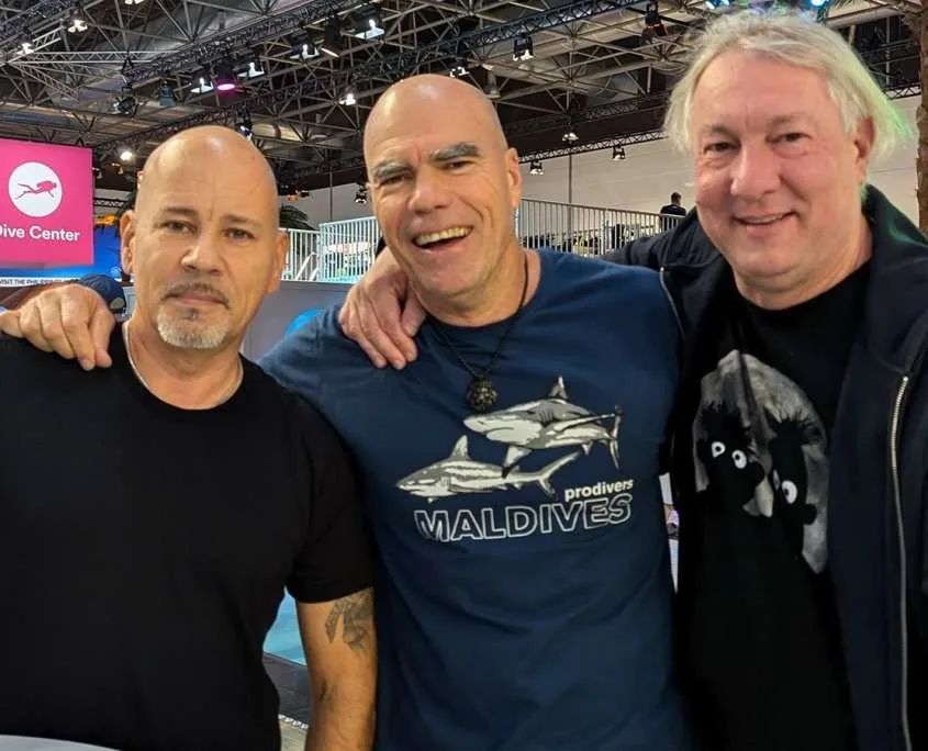 Trois hommes souriants posent ensemble devant un écran avec un logo