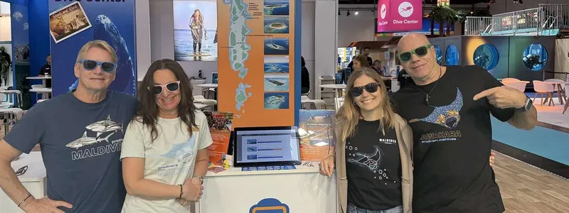 Quatre personnes souriantes posent devant un stand de centre de plongée