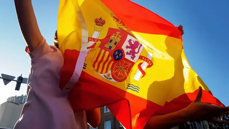 Drapeau espagnol brandi par des mains contre un ciel bleu