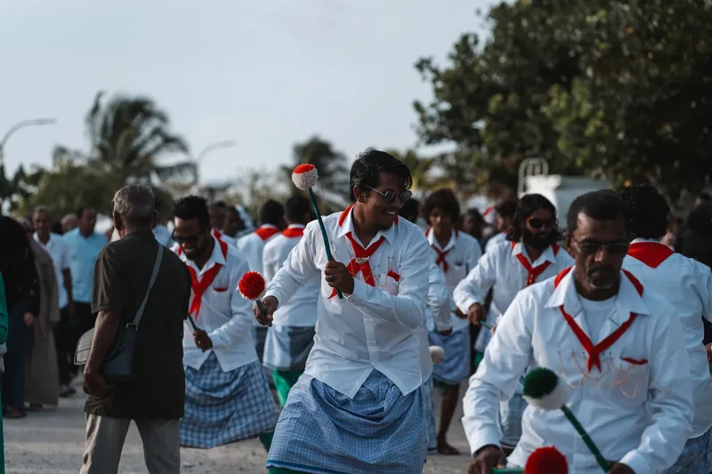 Groupe d'hommes souriants dansant avec des bâtons décorés en extérieur