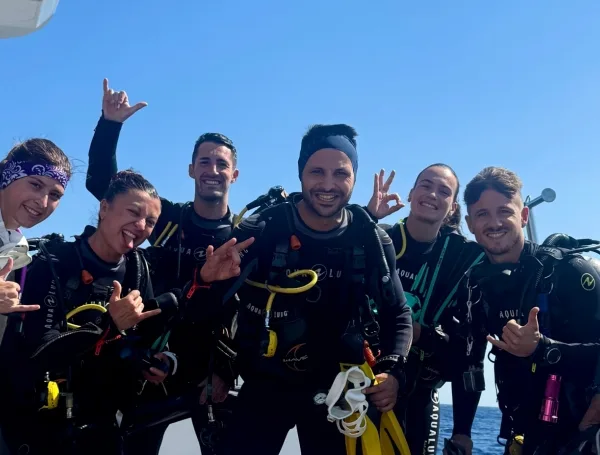Groupe de plongeurs souriants sur un bateau en mer, équipement visible