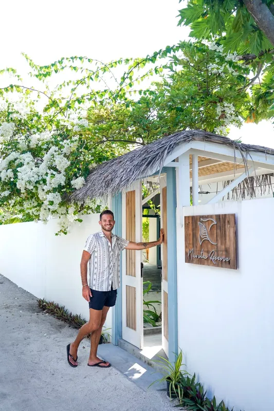 Un homme souriant se tient à l'entrée d'un bâtiment tropical