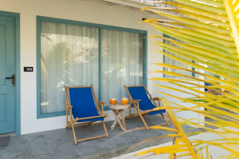Terrasse avec deux chaises longues bleues, une porte turquoise et palmiers