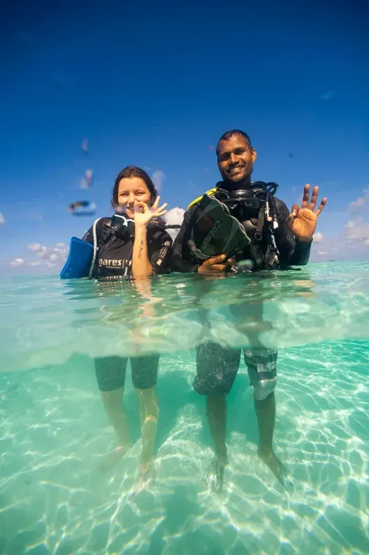 Deux plongeurs souriants font signe dans une eau turquoise claire