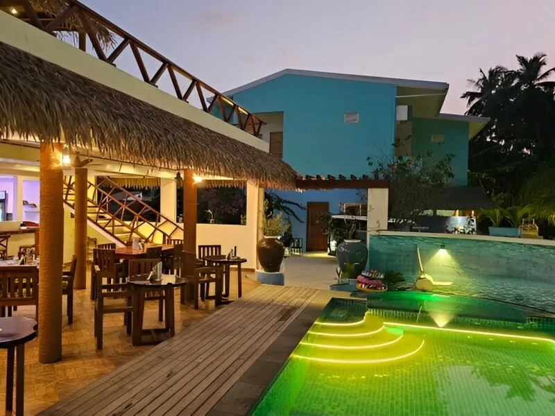 Terrasse avec tables, chaises et piscine illuminée au crépuscule