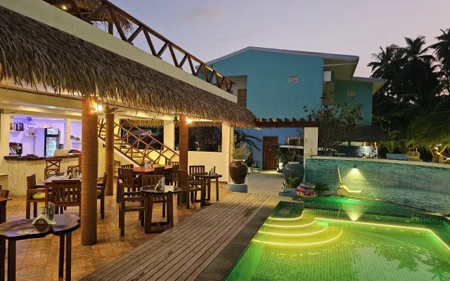 Terrasse avec mobilier, piscine illuminée et bâtiment turquoise au fond