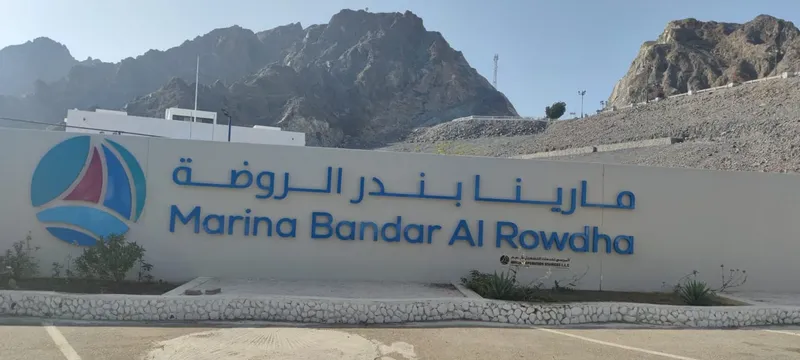 Façade blanche avec logo et nom de la marina, montagnes en arrière-plan