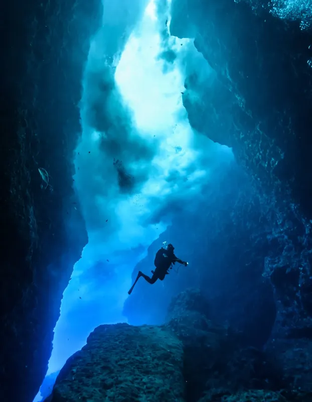 Plongeur explore une grotte sous-marine éclairée par la lumière du soleil