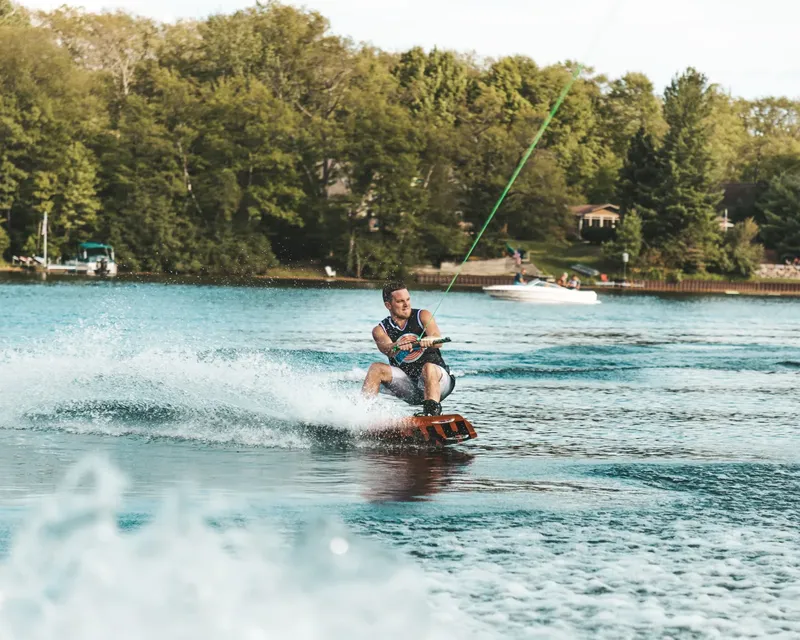 Homme pratiquant le wakeboard sur un lac ensoleillé avec un bateau